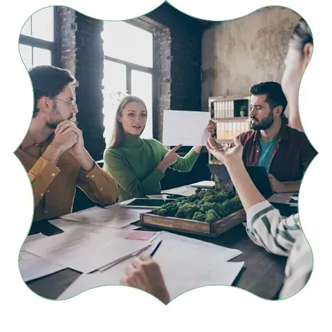 Reunión de equipo alrededor de una mesa, con personas discutiendo bocetos de diseño en una oficina luminosa.
